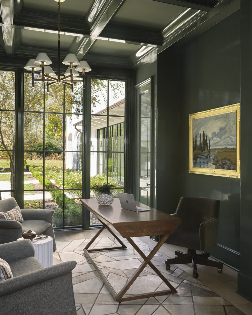Custom luxury home office featuring dark green millwork, a coffered ceiling, oversized windows and designer furnishings.